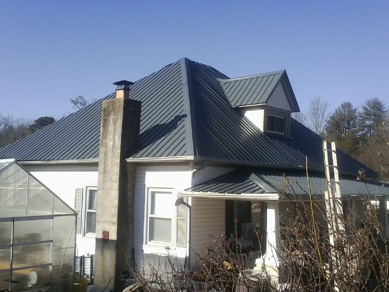 Dark blue standing seam metal roof on a white farmhouse with dormer — Slate & Tile Roof Repair by Roofing Brothers in Tonganoxie
