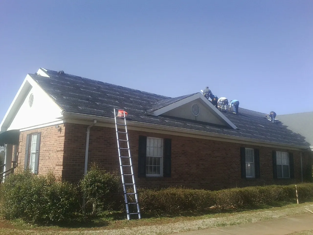 Crew tearing shingles off a brick ranch roof with a ladder set — Metal Roof Repair work by our crew in Tonganoxie