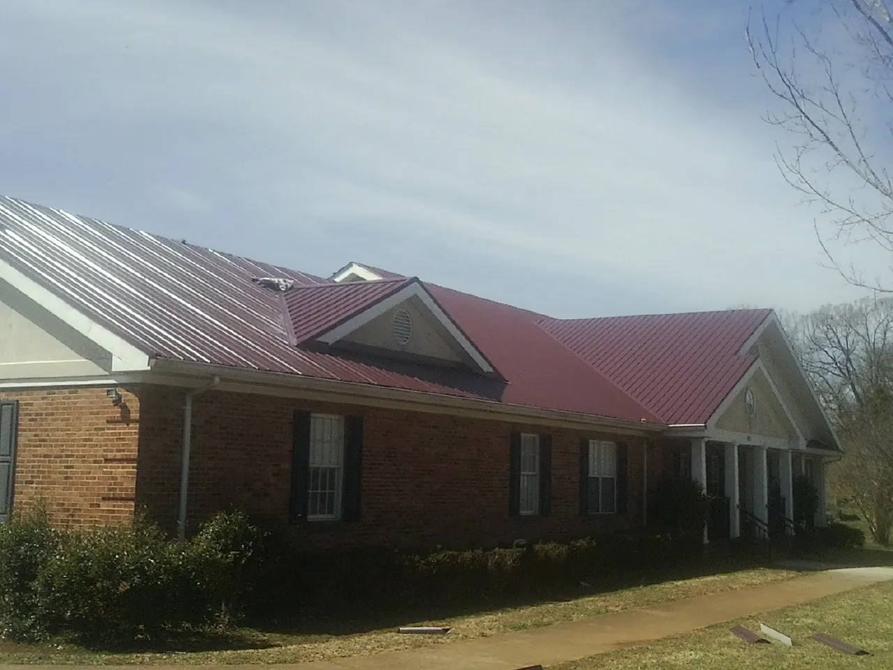 Red metal roof with gabled entries on a long brick building, from a Hail Damage Roof Repair job in Tonganoxie
