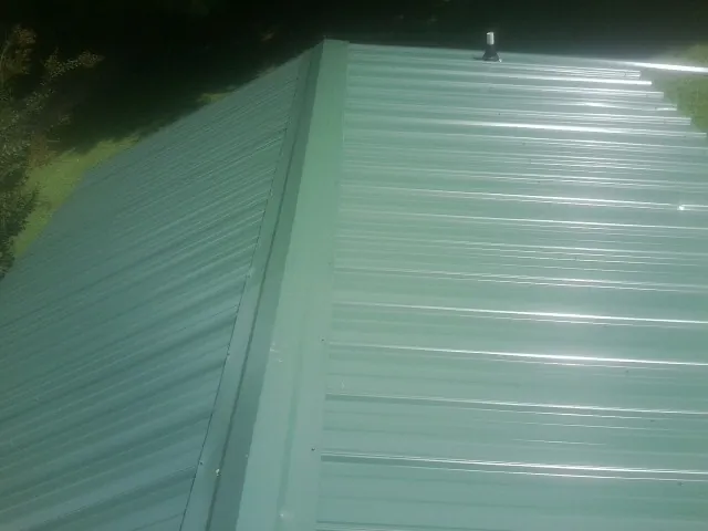 New green metal panels meeting at the ridge of a roof — Flat Roof Repair work by our crew in Tonganoxie