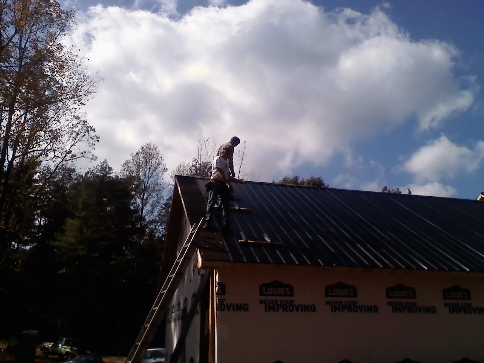 Roofer fastening dark metal panels high against a cloudy sky, from a Roof Inspection job in Tonganoxie