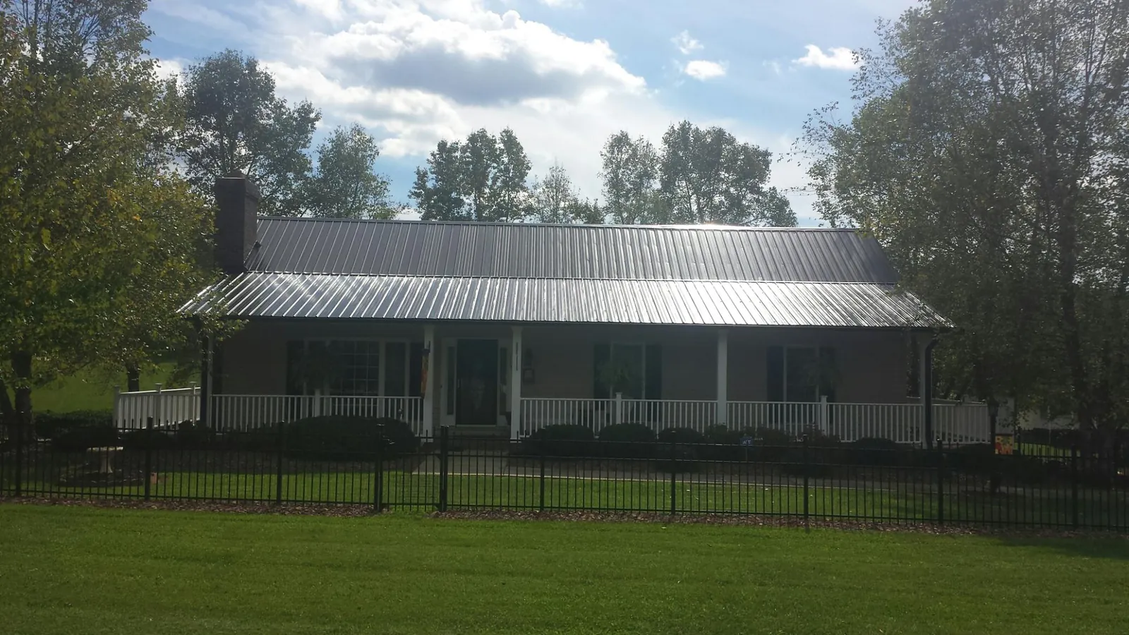 Gray metal roof on a brick ranch with a full width front porch — Gutter Guard Installation work by our crew in Tonganoxie