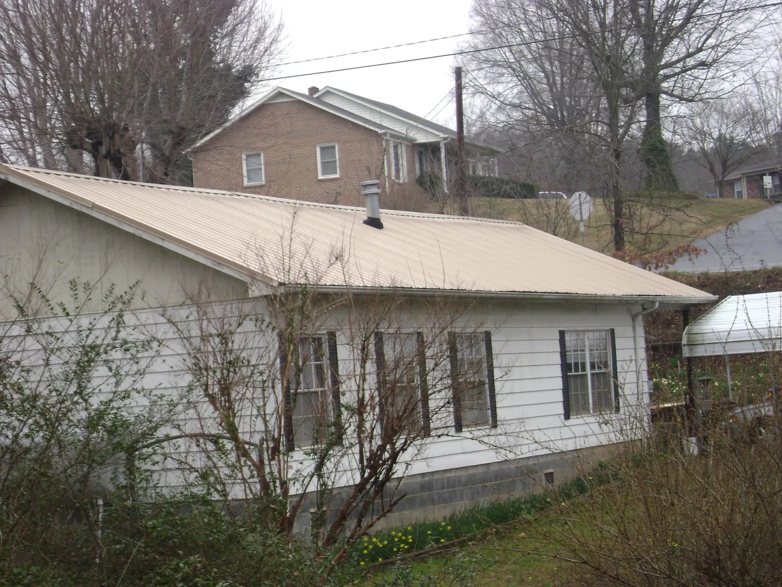 Tan metal roof on a white sided house set into a hillside — Commercial Roofing by Roofing Brothers in Tonganoxie